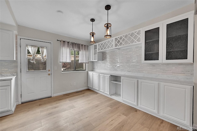 kitchen featuring light wood finished floors, open shelves, white cabinets, glass insert cabinets, and tasteful backsplash