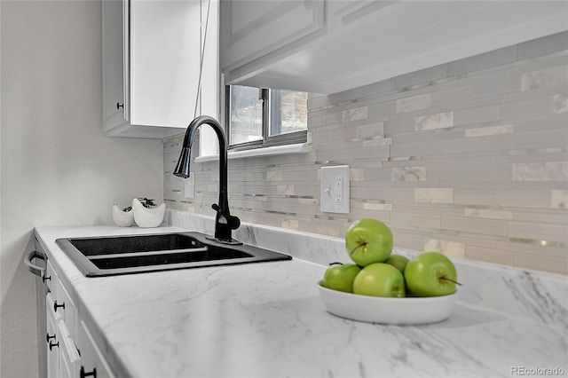 interior details with white cabinets, light stone counters, tasteful backsplash, and a sink