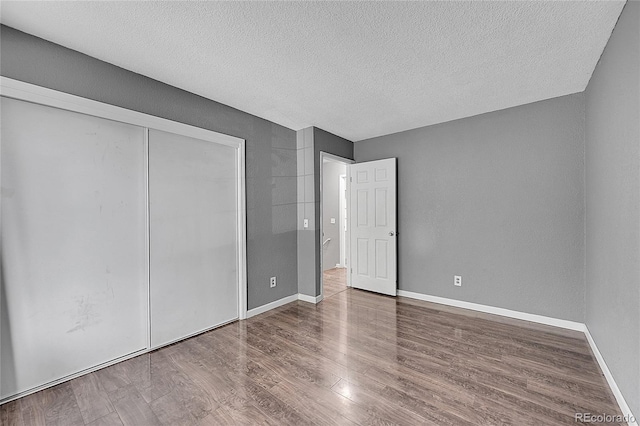 unfurnished bedroom featuring baseboards, wood finished floors, a closet, and a textured ceiling