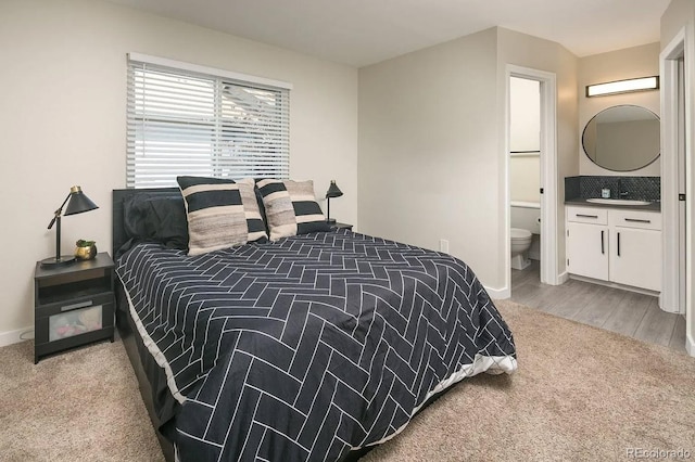 bedroom featuring wood finished floors, a sink, ensuite bath, baseboards, and carpet flooring