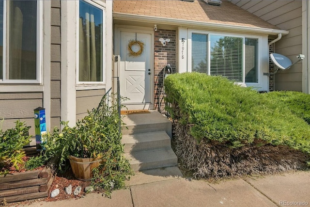 entrance to property featuring brick siding and roof with shingles