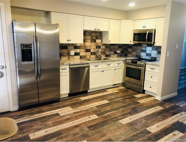 kitchen with white cabinets, light stone counters, dark wood-type flooring, stainless steel appliances, and a sink