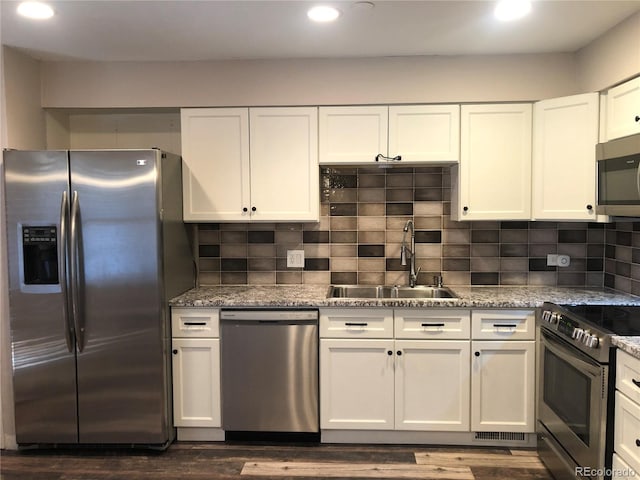 kitchen featuring light stone counters, tasteful backsplash, appliances with stainless steel finishes, white cabinets, and a sink