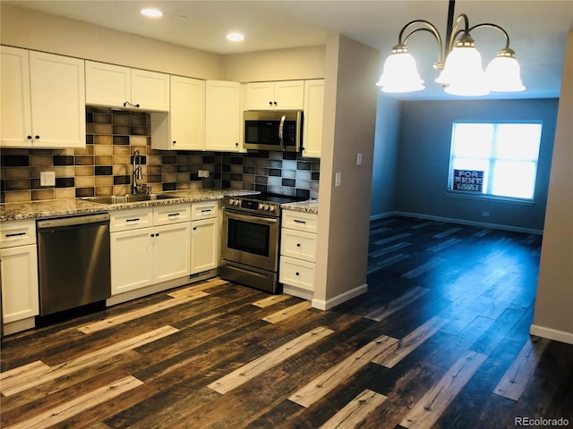 kitchen featuring light stone counters, hanging light fixtures, appliances with stainless steel finishes, white cabinets, and a sink