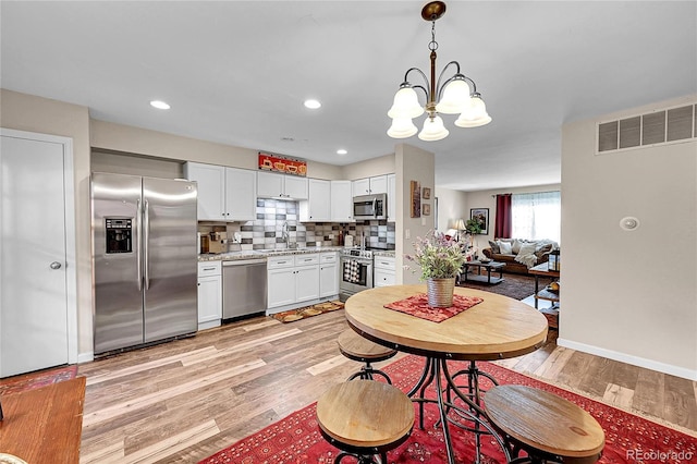 interior space with a notable chandelier, a sink, light wood finished floors, stainless steel appliances, and visible vents