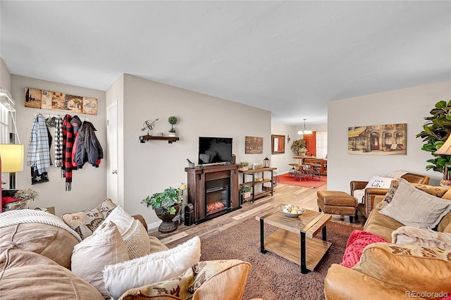 living room featuring a glass covered fireplace, baseboards, light wood-type flooring, and a notable chandelier