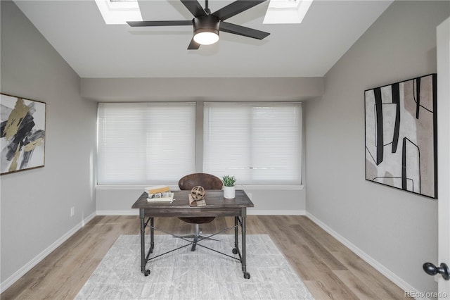 office space featuring lofted ceiling with skylight, ceiling fan, and light wood-type flooring