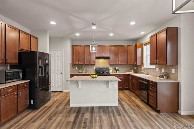 kitchen with a center island, a kitchen breakfast bar, wood-type flooring, decorative light fixtures, and black appliances