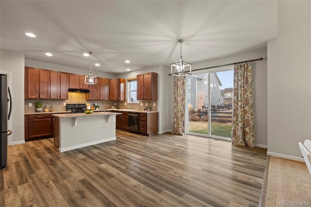 kitchen with pendant lighting, a breakfast bar, a center island, black appliances, and dark hardwood / wood-style flooring