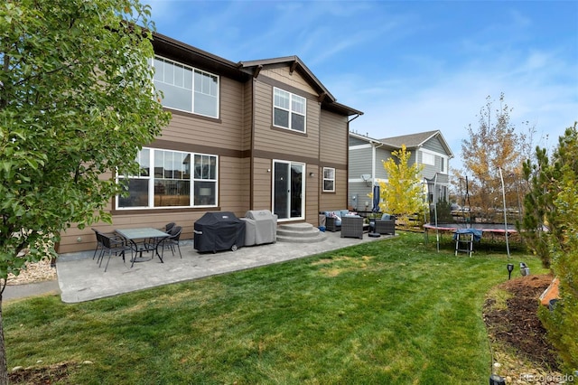 rear view of property featuring a lawn, a patio, and a trampoline