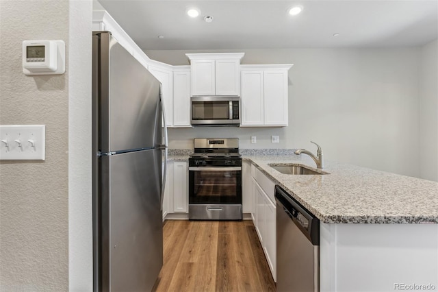 kitchen featuring sink, light hardwood / wood-style flooring, appliances with stainless steel finishes, light stone counters, and white cabinetry