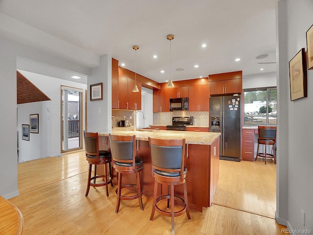 kitchen with light hardwood / wood-style flooring, pendant lighting, black appliances, decorative backsplash, and sink