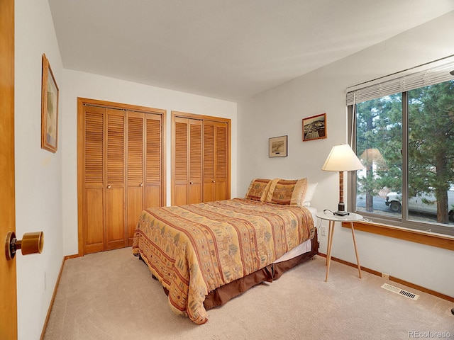 bedroom with multiple closets and light carpet