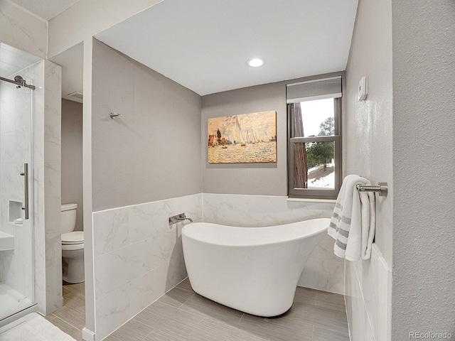 bathroom featuring toilet, separate shower and tub, and tile walls