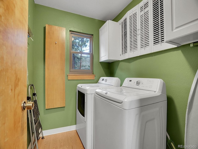 washroom featuring washing machine and clothes dryer, cabinets, and light hardwood / wood-style flooring