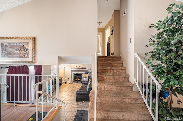 stairway featuring a warm lit fireplace and tile patterned floors