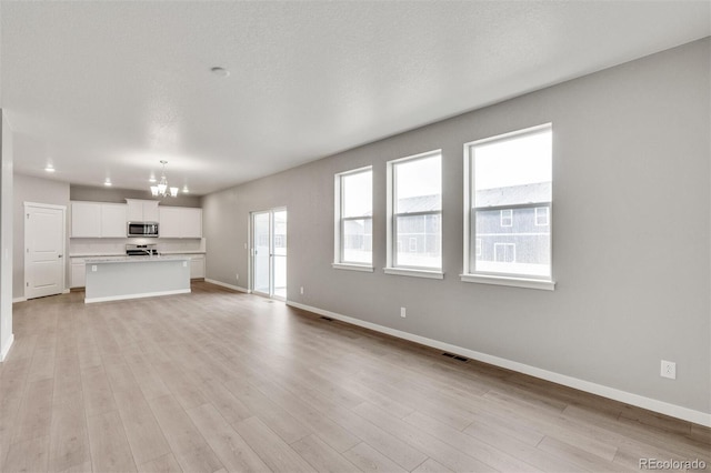 unfurnished living room featuring light hardwood / wood-style floors, a textured ceiling, and a notable chandelier