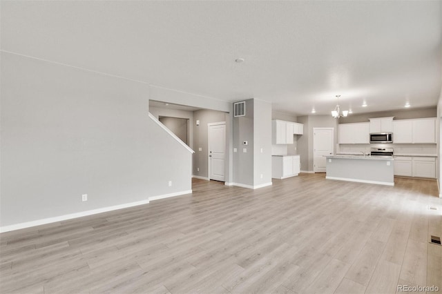 unfurnished living room featuring an inviting chandelier and light hardwood / wood-style flooring