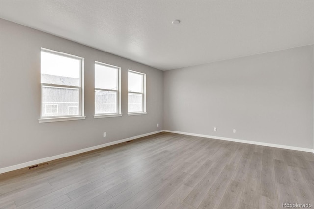 spare room featuring a textured ceiling and light hardwood / wood-style floors