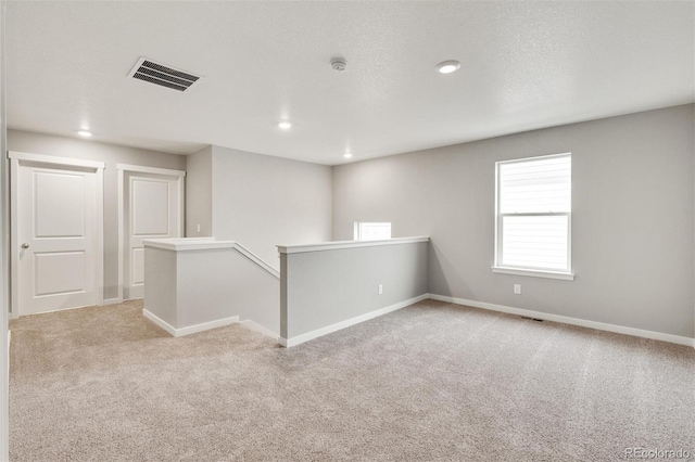 spare room featuring light colored carpet and a textured ceiling