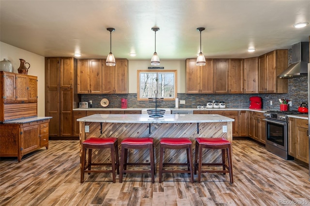 kitchen with stainless steel gas stove, a kitchen island, hanging light fixtures, and wall chimney exhaust hood