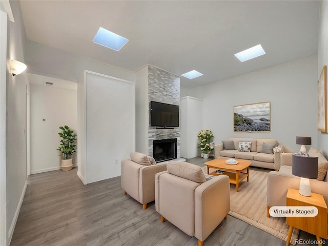 living area with a skylight, a fireplace, baseboards, and light wood-style flooring