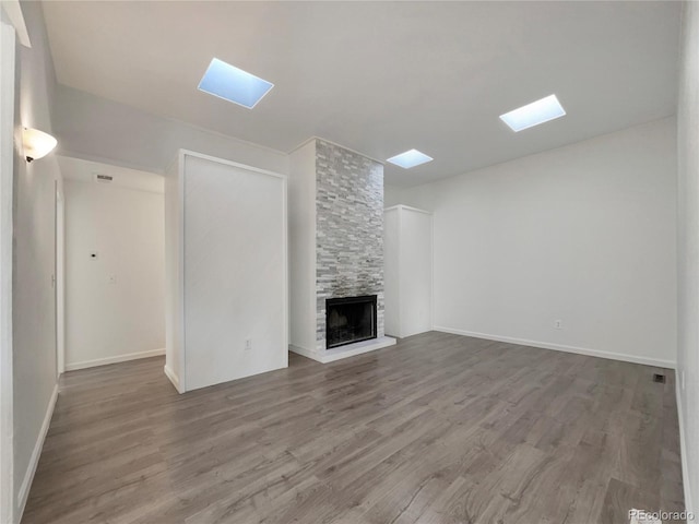 unfurnished living room with a fireplace, a skylight, baseboards, and wood finished floors