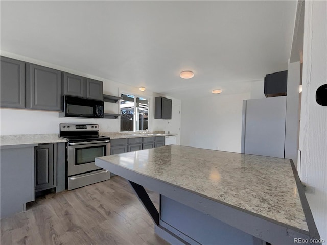 kitchen featuring gray cabinetry, black microwave, light wood-style flooring, freestanding refrigerator, and electric range