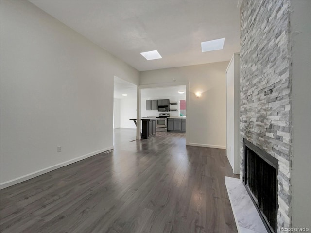 unfurnished living room with a stone fireplace, dark wood-type flooring, a skylight, and baseboards