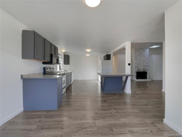 kitchen featuring light wood-type flooring, freestanding refrigerator, black microwave, a fireplace, and stainless steel electric range oven