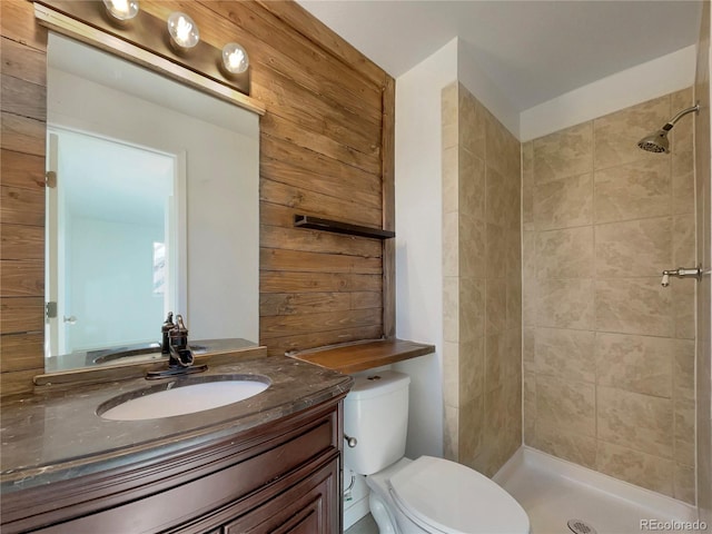 bathroom featuring a tile shower, toilet, vanity, and wood walls