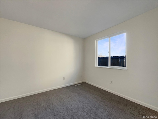 spare room featuring visible vents, baseboards, and dark carpet