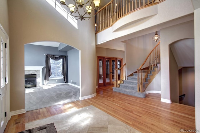 foyer featuring a towering ceiling, hardwood / wood-style floors, a high end fireplace, and a chandelier