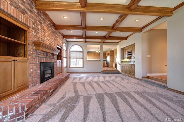 unfurnished living room with coffered ceiling, a brick fireplace, carpet floors, and beamed ceiling