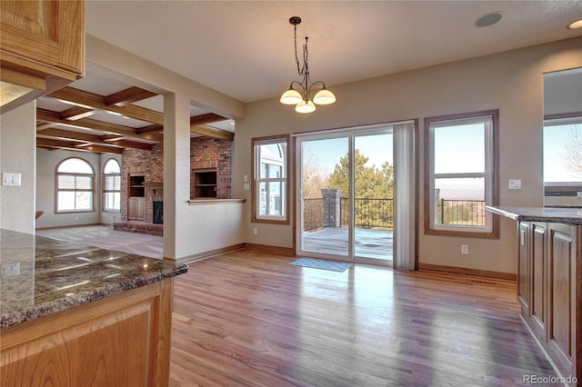 interior space featuring coffered ceiling, decorative light fixtures, a brick fireplace, light hardwood / wood-style flooring, and dark stone counters