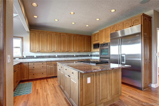 kitchen with built in appliances, light stone countertops, light hardwood / wood-style floors, and a kitchen island