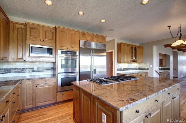 kitchen featuring pendant lighting, light hardwood / wood-style flooring, a center island, built in appliances, and decorative backsplash