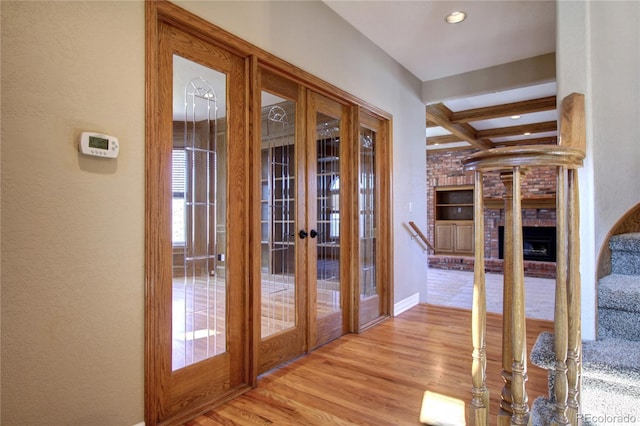 doorway to outside featuring french doors, a fireplace, beam ceiling, and light hardwood / wood-style flooring