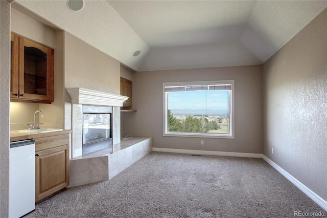 unfurnished living room featuring a tiled fireplace, lofted ceiling, sink, and light colored carpet