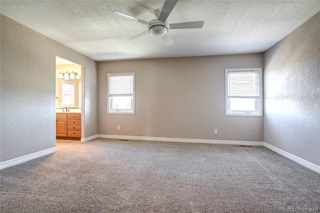 carpeted empty room with ceiling fan, plenty of natural light, sink, and a textured ceiling