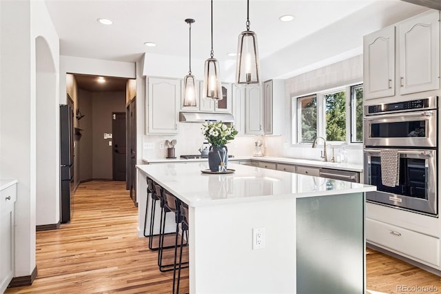 1570 Blakcomb Ct, Evergreen, CO 80439 - kitchen featuring appliances with stainless steel finishes, a kitchen bar, under cabinet range hood, a kitchen island, and light wood finished floors