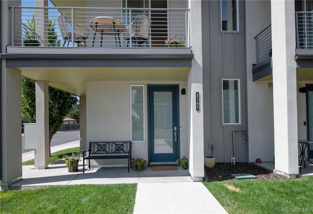 property entrance with board and batten siding, a balcony, and stucco siding