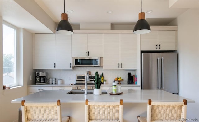 kitchen with light countertops, appliances with stainless steel finishes, decorative backsplash, and a center island with sink