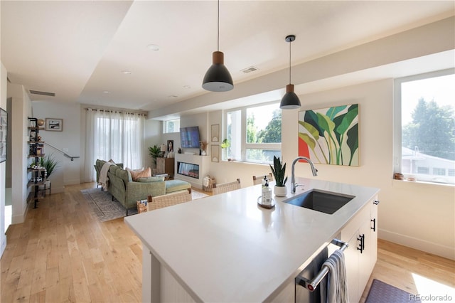 kitchen featuring visible vents, a glass covered fireplace, a sink, and light wood-style floors