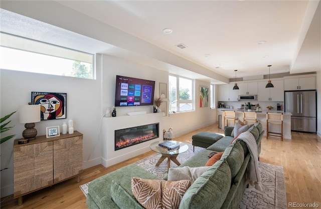 living room with baseboards, visible vents, a glass covered fireplace, and light wood-style flooring