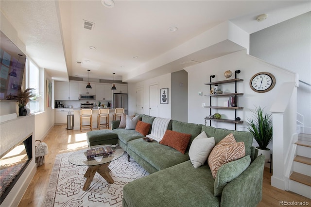 living area featuring stairs, visible vents, and light wood-style floors