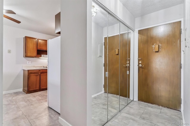 interior space featuring light tile patterned flooring, a textured ceiling, baseboards, and ceiling fan