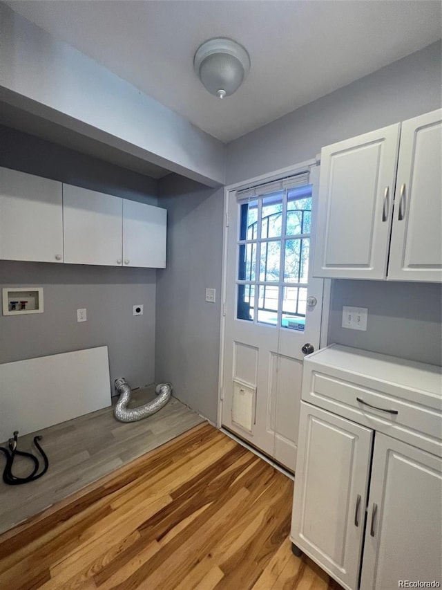 clothes washing area featuring hookup for an electric dryer, washer hookup, light hardwood / wood-style floors, and cabinets