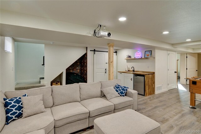 living room with wet bar, light hardwood / wood-style flooring, and a barn door