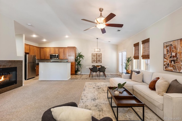 living room featuring vaulted ceiling, ceiling fan, light colored carpet, and a tile fireplace